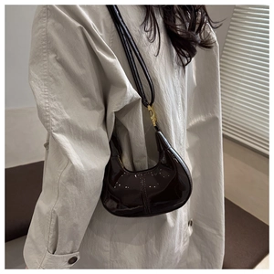 Détail du sac croissant en cuir verni noir brillant avec boucle en métal doré sur la bandoulière