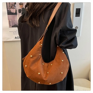 Brown suede crescent bag with gold stud details worn by a model in a minimal setting