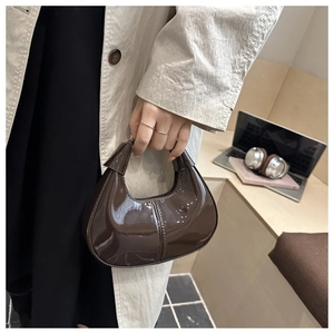 Détail du sac demi-lune en cuir verni marron brillant tenu par un mannequin au bureau