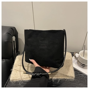 Detail of black suede bucket bag featuring embossed text and gold-tipped knotted shoulder strap