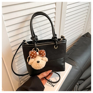 Detail der schwarzen Beuteltasche mit Teddybär-Anhänger und gemischter Materialstruktur