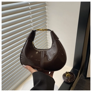 Detail of dark brown glossy patent leather crescent bag with gold handle and strap