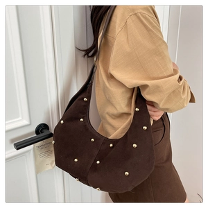Model shot of a dark brown suede crescent bag with gold rivets and leather strap