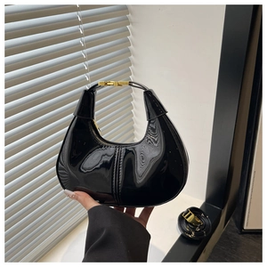 Detail of glossy black patent leather crescent bag with golden clasp and long strap