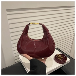 Gros plan du sac croissant en cuir verni bordeaux brillant avec boucle en métal doré