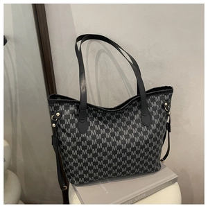 Detail of trendy tote bag featuring repeating M patterns and sleek black leather straps