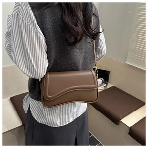 Detailed view of the dark brown crossbody bag featuring a unique wavy flap and golden hardware