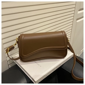 Detail view of a brown leather bag with a wavy flap on a book in a minimalist setting