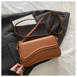 Detail of caramel leather crossbody bag with asymmetric curved flap and gold metal hooks