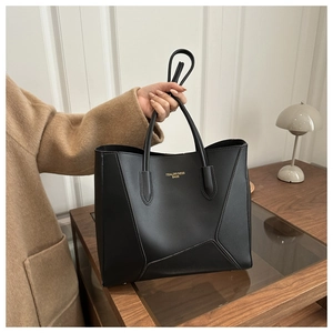 Detail of black leather tote bag featuring gold logo and geometric stitching accents