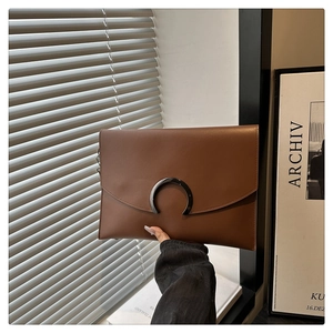 Macro detail of brown leather envelope clutch with a unique C-shaped metal lock clasp