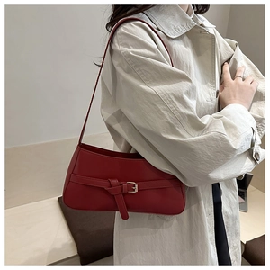 Detail view of red leather underarm bag with decorative belt buckle on beige trench coat