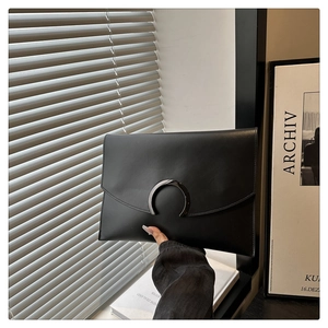 Detail of a black leather envelope clutch featuring a minimalist metal horseshoe buckle