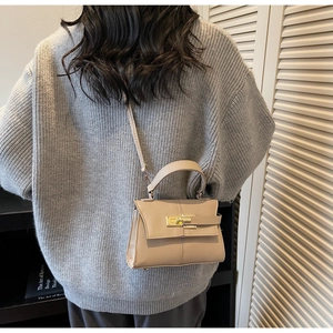 Detail of beige textured leather handbag with gold metal lock worn by a model in soft light