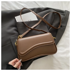 Detail of a brown leather crossbody bag with curved flap and golden metal hardware