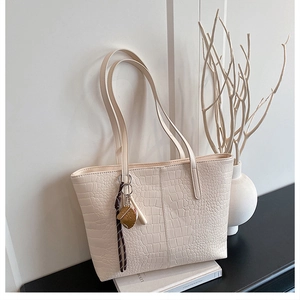 Detail of cream crocodile embossed tote bag with vertical stitching and decorative charm