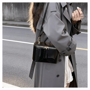 Outdoor street shot of a black patent leather box bag with a gold chain strap