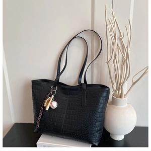 Detail of a black crocodile pattern tote bag with baseball themed pendants on a table