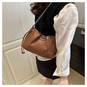 Détail d'un sac bandoulière marron plissé avec chaîne argentée porté par un modèle
