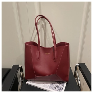 Detail of burgundy leather tote bag with gold branding placed on a minimalist chair