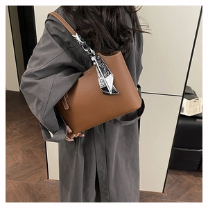 Brown leather tote bag with geometric silk scarf detail shown on shoulder with grey coat