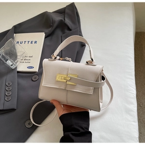 Close-up of off-white lychee grain leather handbag with gold metal lock and flap cover
