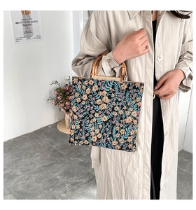 Floral canvas tote bag with bamboo handles shown being carried by a model in a trench coat