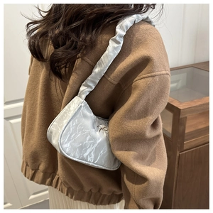Silberne Schultertasche mit Plisseestruktur und Metallelementen von Model getragen