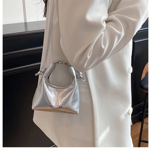 Silver metallic crossbody bag with round metal handle shown on a white suit model