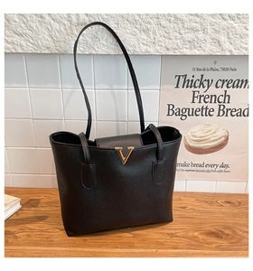 Detail of black tote bag with lychee pattern texture and golden V logo on wooden surface