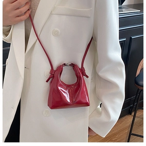 Detail of red patent leather mini crossbody bag with glossy finish and brand logo