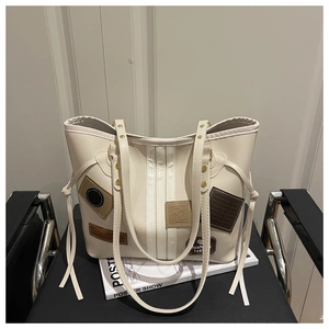 Detail of cream tote bag with vintage patches and slender straps on a leather chair
