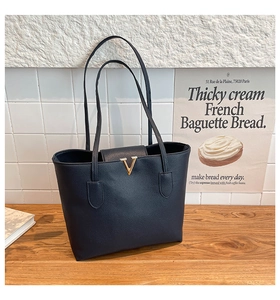 Detail of black pebbled leather tote bag featuring a golden V-shaped metal logo buckle