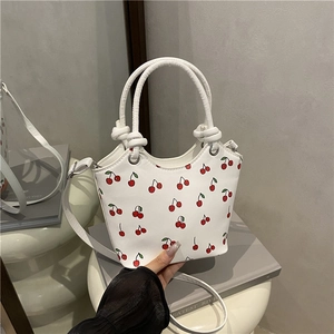 Chic white bucket bag with red cherry print featuring a braided handle and shoulder strap