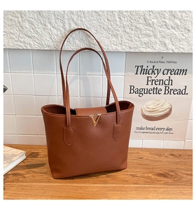 Detail of classic brown tote bag with litchi grain texture and golden V-shaped metal hardware