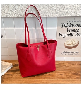 Detail of red pebbled leather tote bag with gold V-shape metal buckle on wooden surface