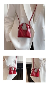 Detailed view of red glossy leather crossbody bag with letter logo and shoulder strap