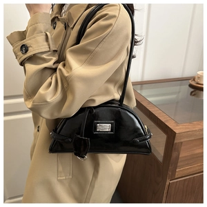 Detail of black patent leather crescent shoulder bag with silver plaque on khaki trench coat