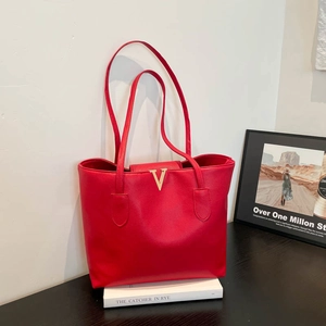 Classic red pebble leather tote bag with gold V buckle on book in minimalist setting