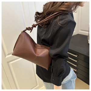 Detail of minimalist dark brown leather shoulder bag with cylinder strap and knot feature