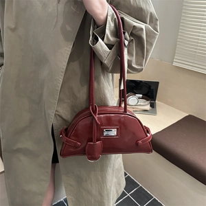 Deep red crescent underarm bag with glossy finish shown on model in urban office setting