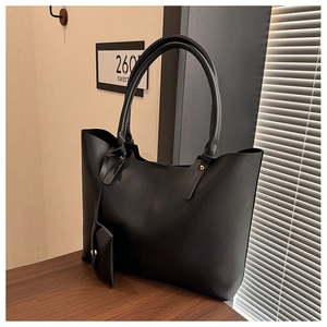 Detail of a matte black tote bag with side coin pouch on a minimalist desktop