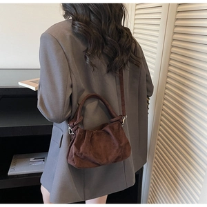 Detailed view of dark brown suede crossbody bag with pleated texture and knotted handle