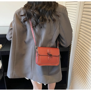Detail of red-brown crossbody bag featuring horn buckle closure and contrast stitching