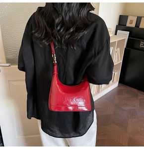 Detail of red glossy shoulder bag featuring embossed maison text and adjustable strap