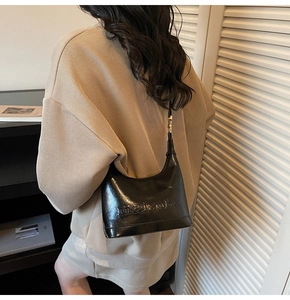 Glossy black patent leather bag with embossed lettering and adjustable gold strap