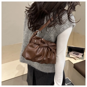 Detail der dunkelbraunen Ledertasche mit seitlicher Schleife und Falten-Design am Model