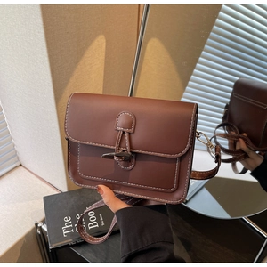 Detailed view of the brown leather messenger bag with toggle closure and white contrast stitching