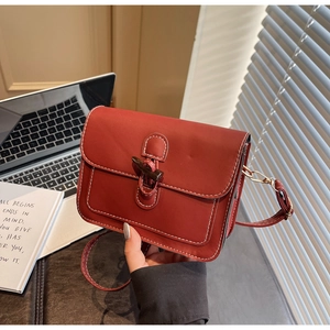 Detail of brick red retro crossbody bag with wooden toggle closure and white stitching