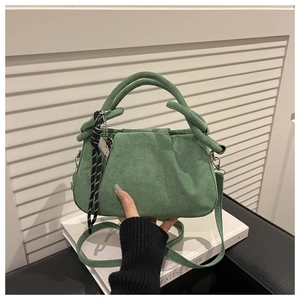 Detail of dark green suede handbag featuring dual handles and woven rope pendant charm